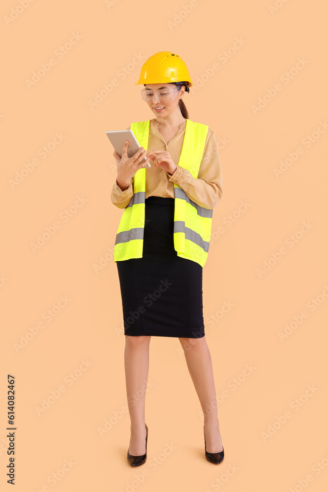 Female engineer in vest and with tablet computer on beige background