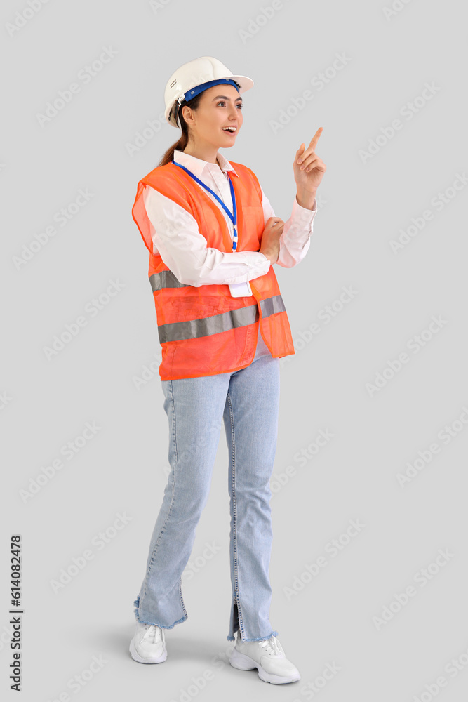 Female worker in vest pointing at something on light background