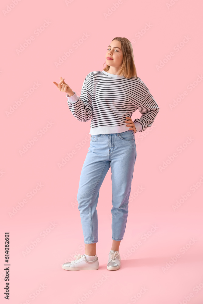 Young woman in striped sweatshirt snapping fingers on pink background