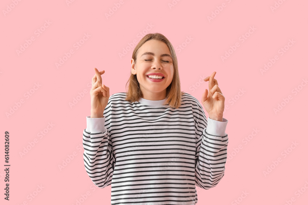 Happy young woman in striped sweatshirt crossing fingers on pink background