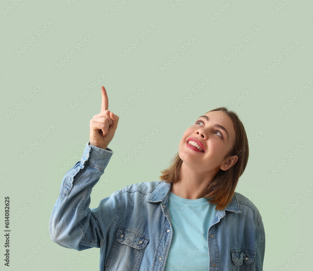 Young woman in denim shirt pointing at something on green background