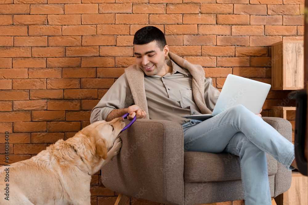 Young man with laptop and cute Labrador dog sitting in office