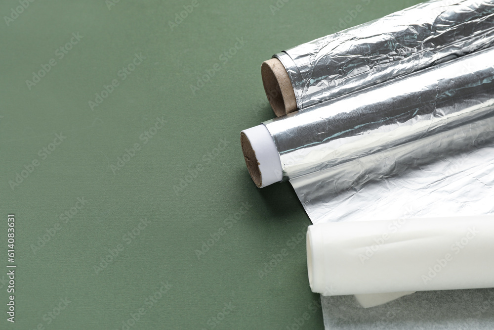 Rolls of aluminium foil and baking paper on color background