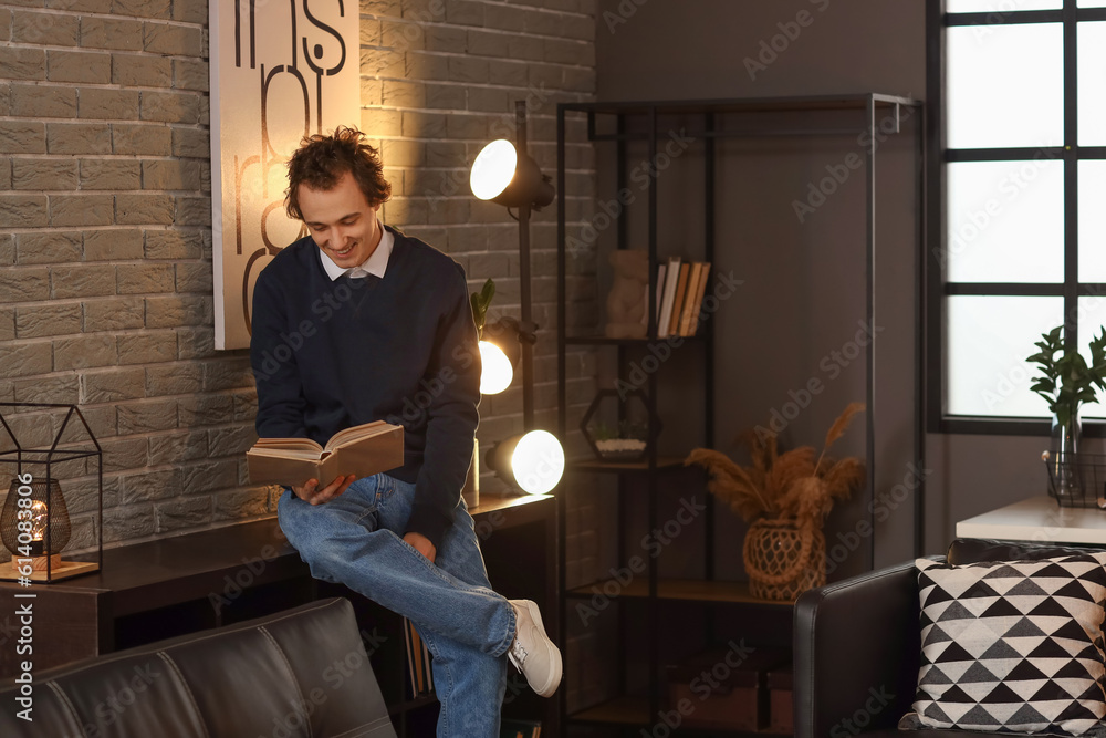 Young man reading book at home late in evening