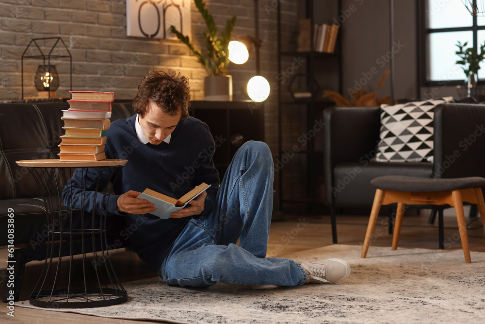 Young man reading book at home late in evening