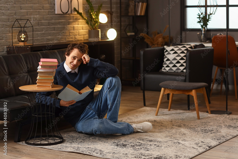 Young man reading book at home late in evening