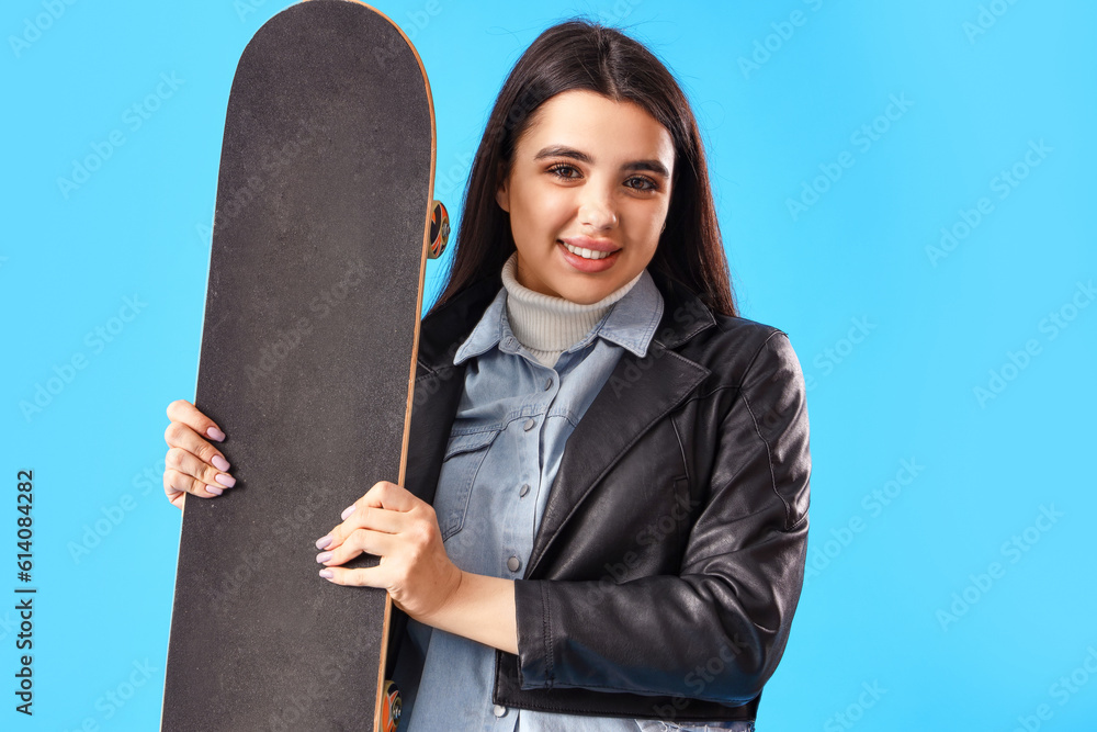 Stylish young woman with skateboard on blue background