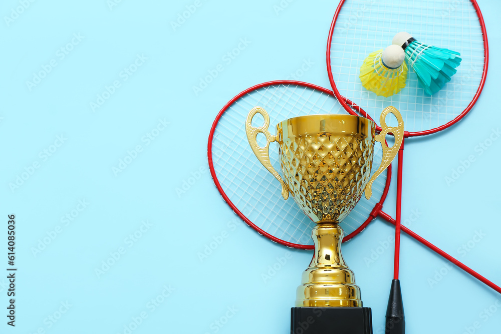 Gold cup with badminton rackets and shuttlecocks on blue background