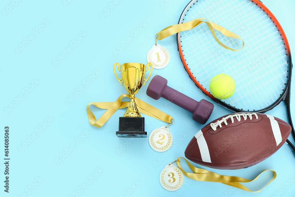 Gold cup with prize medals and sports equipment on blue background