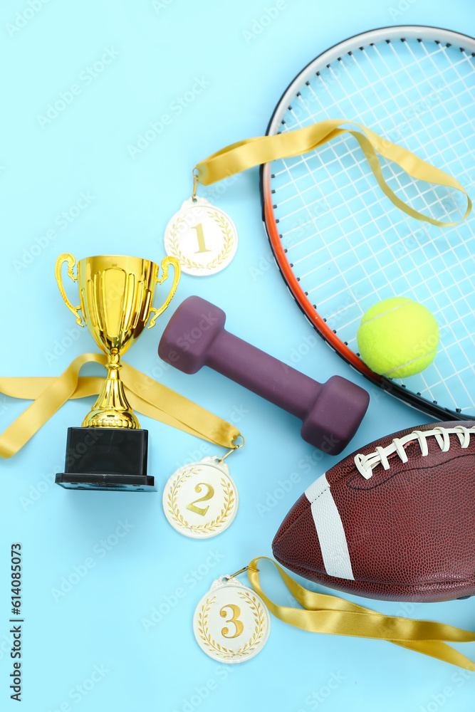 Gold cup with prize medals and sports equipment on blue background