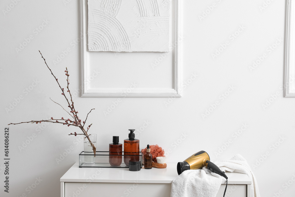 Bath accessories and vase with blooming tree branches on shelf near light wall