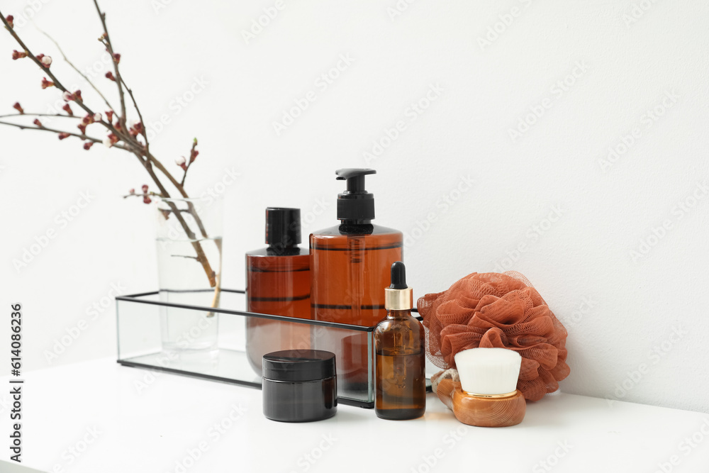 Bath accessories and vase with blooming tree branches on shelf near light wall