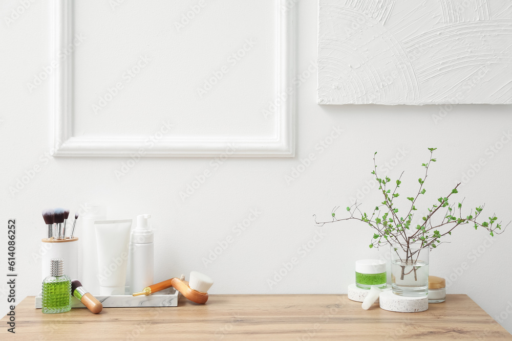 Bath accessories and vase with tree branches on table near light wall