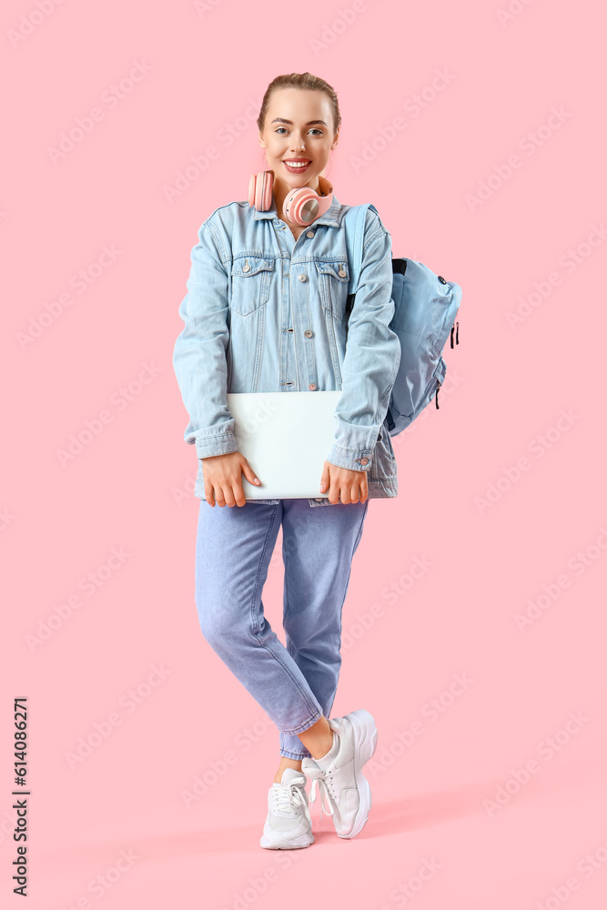 Female student with laptop on pink background