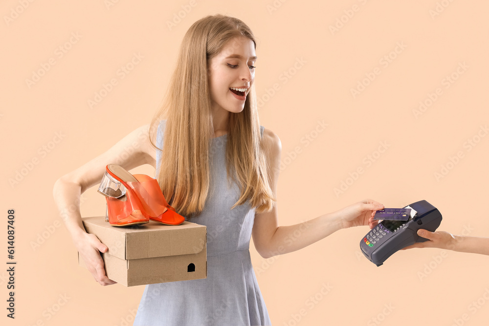 Young woman with shoes and credit card paying on beige background