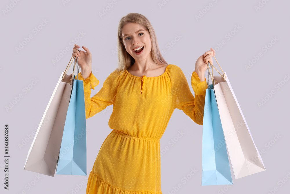 Young woman with shopping bags on light background