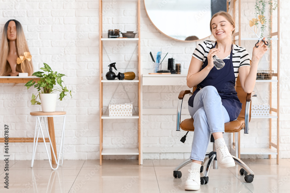 Female hairdresser with scissors and spray in beauty salon