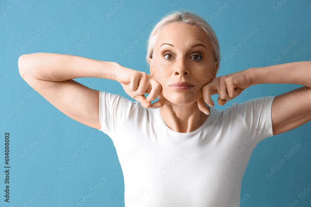 Mature woman doing face building exercise on blue background