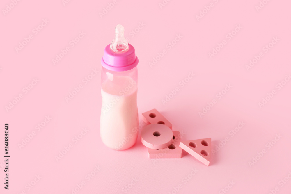 Bottle of milk for baby with toys on pink background