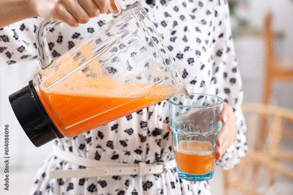 Young woman pouring vegetable juice from blender into glass in kitchen, closeup