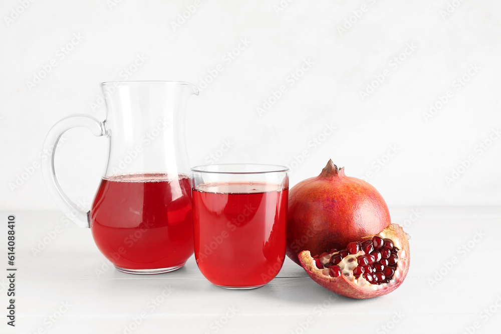 Jug and glass of fresh pomegranate juice on white wooden table