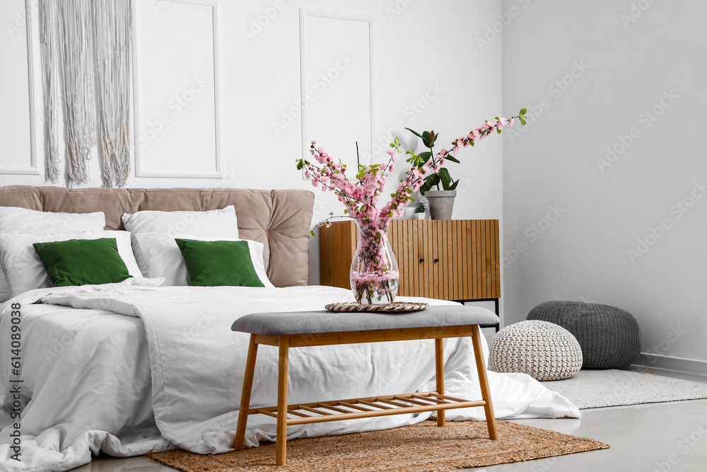 Vase with blooming sakura branches on bedside bench in interior of bedroom