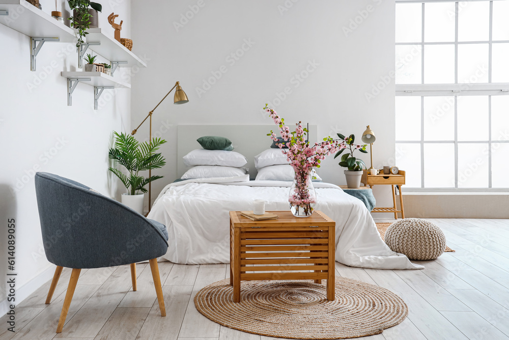 Interior of stylish bedroom with blooming tree branches in vase on wooden table