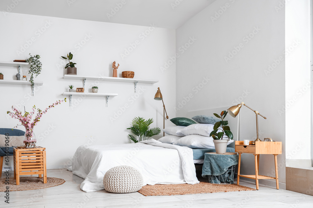 Interior of stylish bedroom with blooming tree branches in vase on wooden table