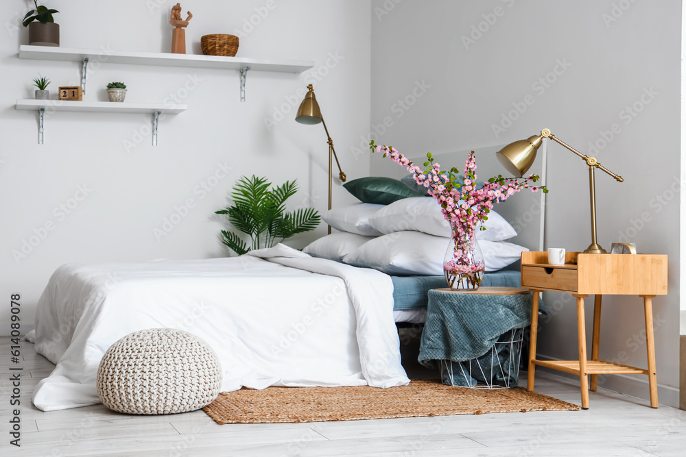 Interior of stylish bedroom with blooming tree branches in vase on bedside table