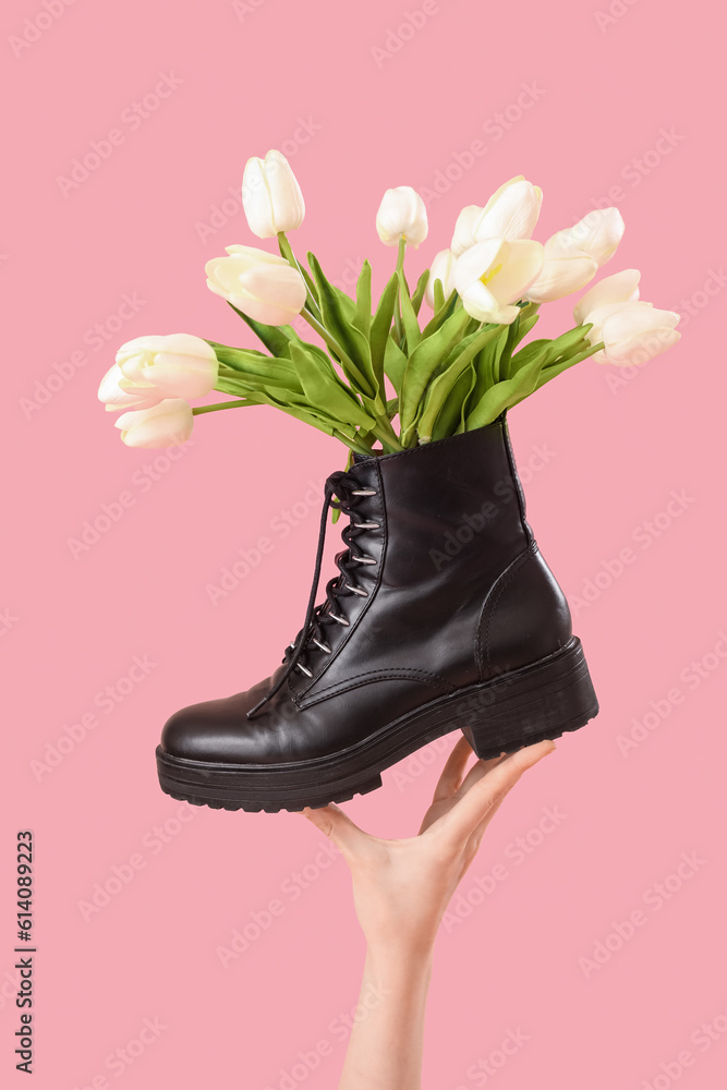 Female hand with tulip flowers in shoes on pink background