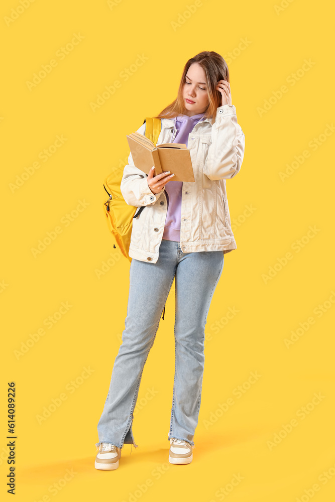 Female student reading book on yellow background