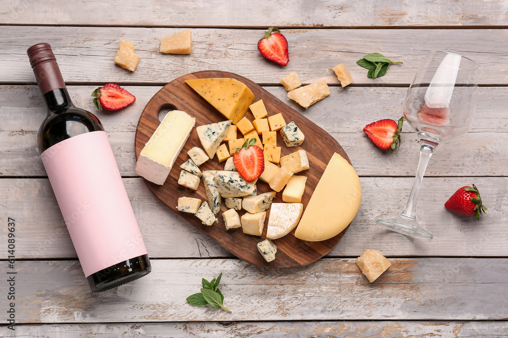 Pieces of tasty cheese, glass and bottle with wine on light wooden background