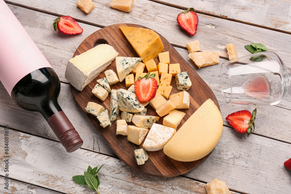 Pieces of tasty cheese, glass and bottle with wine on light wooden background