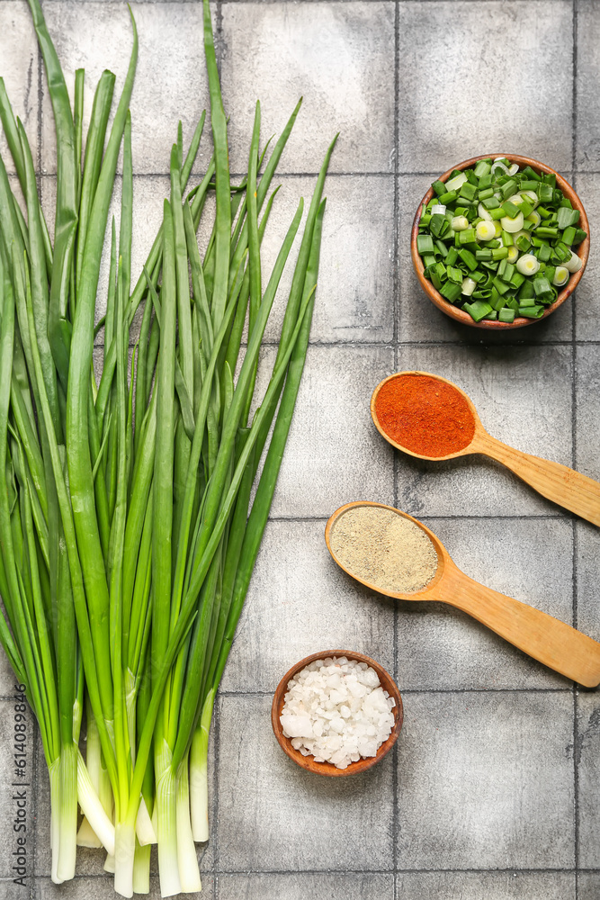 Fresh green onion and spoons with spices on dark tile background