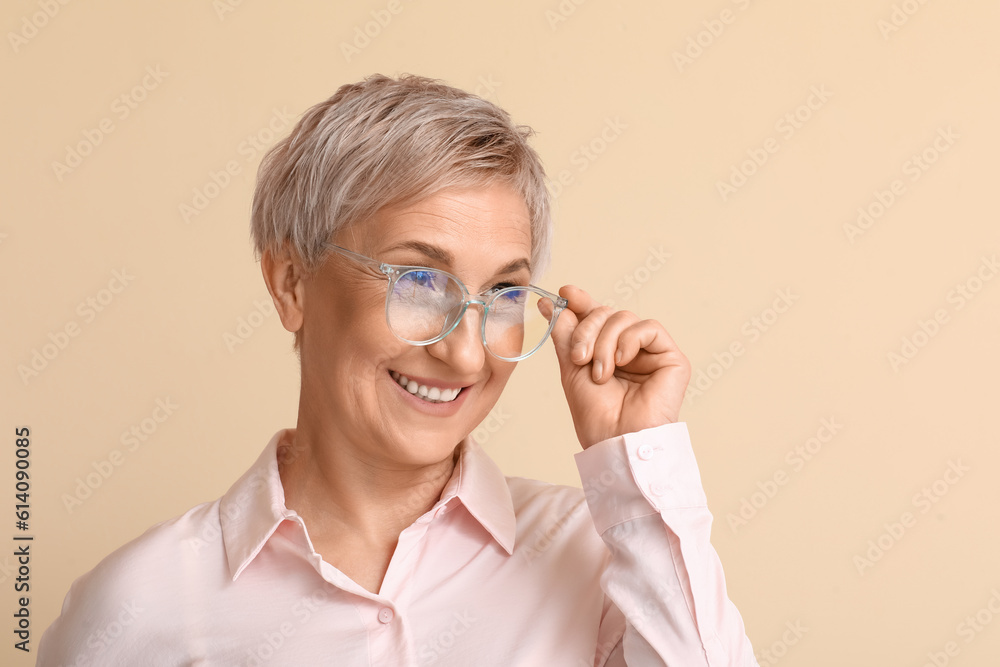 Mature blonde woman in eyeglasses on beige background, closeup