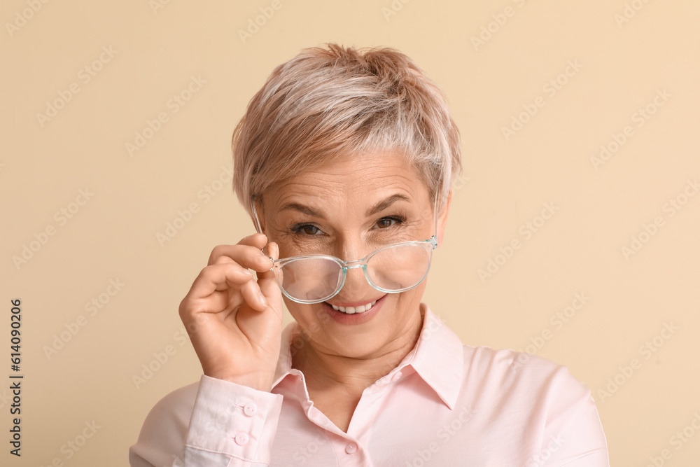 Mature blonde woman in eyeglasses on beige background, closeup