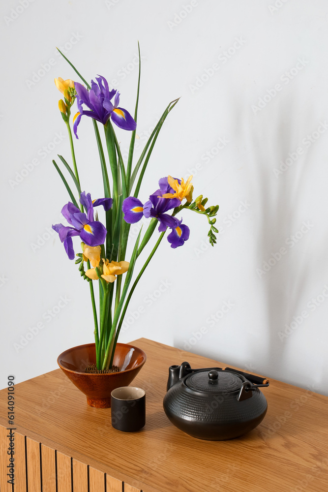 Beautiful ikebana with teapot and cup on table near light wall