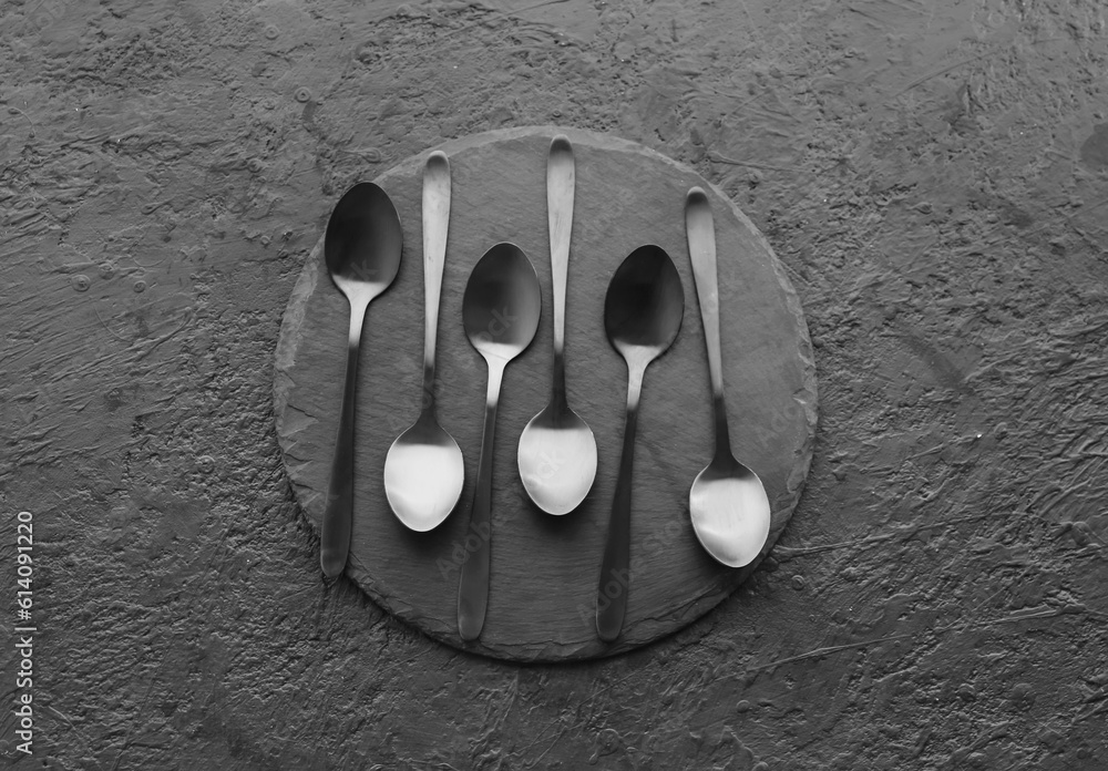 Board with stainless steel spoons on black background