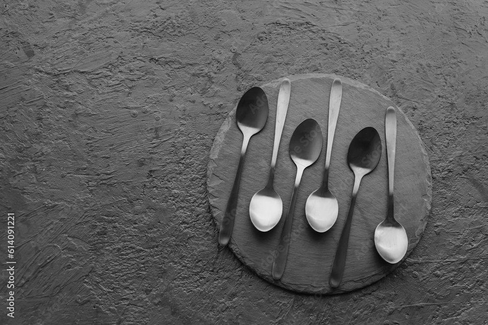 Board with stainless steel spoons on black background