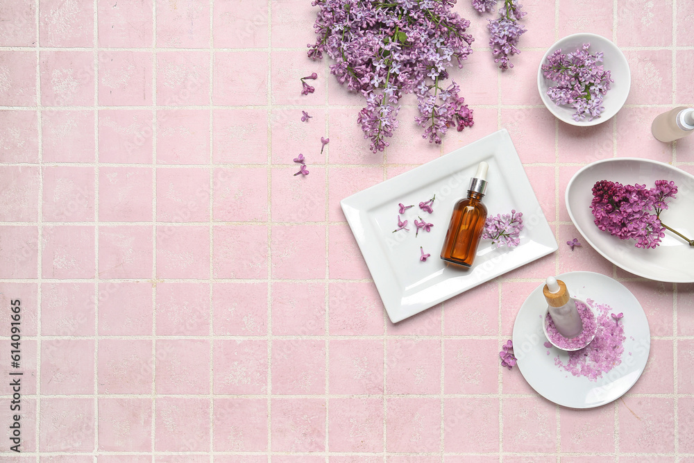 Composition with bottles of lilac essential oil, sea salt and flowers on pink background