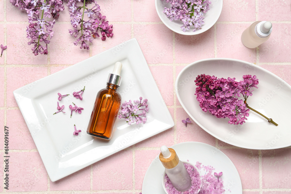 Composition with bottles of lilac essential oil, sea salt and flowers on pink background