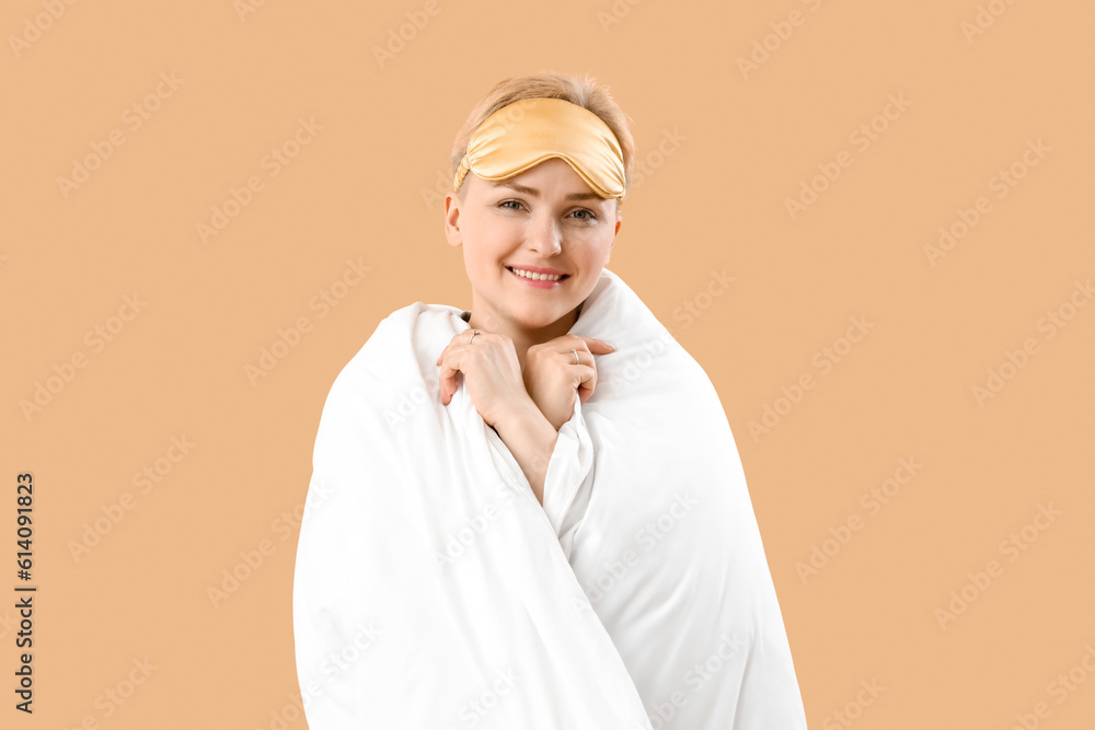 Young woman with sleeping mask and blanket on beige background