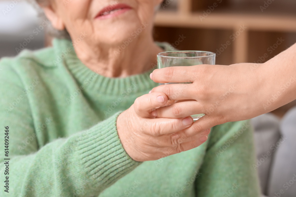 Young woman giving glass of water to her grandmother at home, closeup