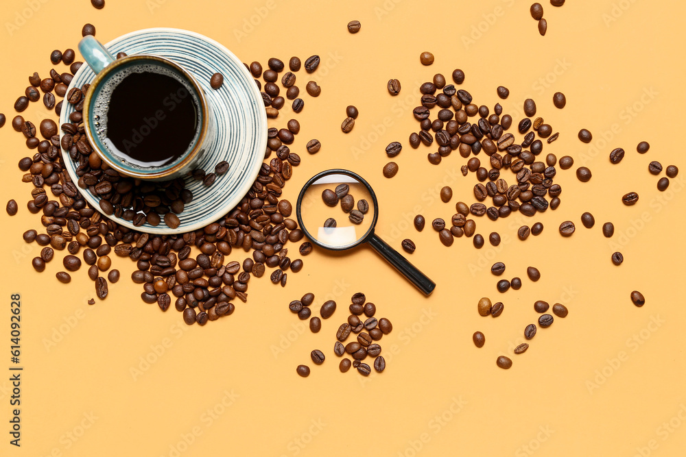 Magnifier and cup of coffee with beans on pale orange background