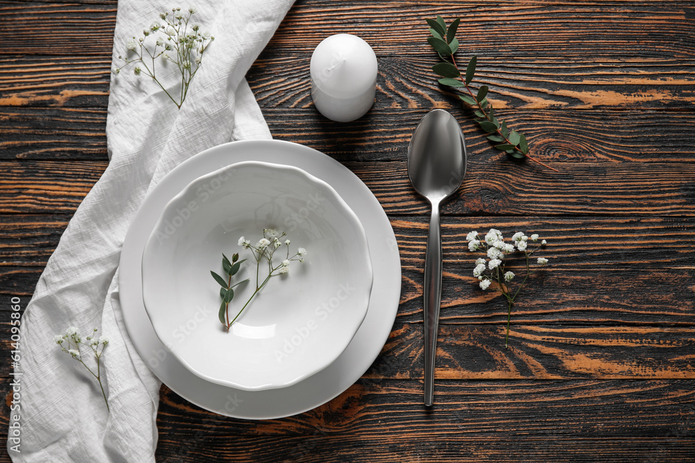 Plates with spoon, flowers and candle on brown wooden background