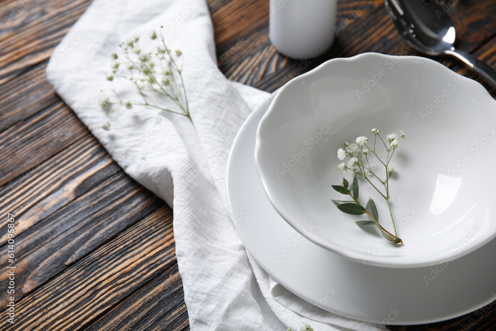 Plates with spoon, flowers and candle on brown wooden background