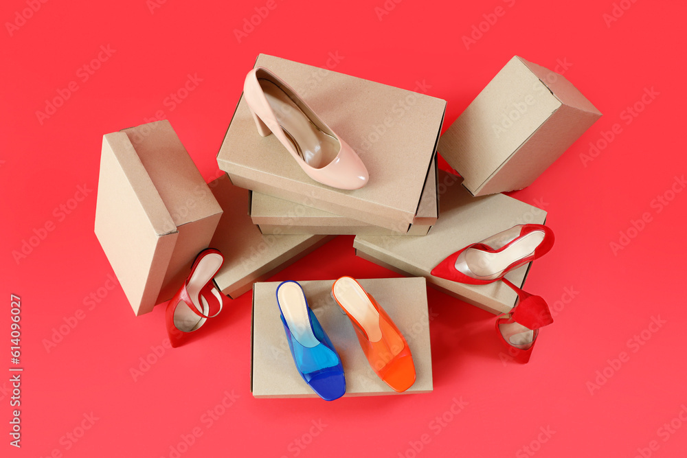 Cardboard boxes with different stylish high-heeled shoes on red background