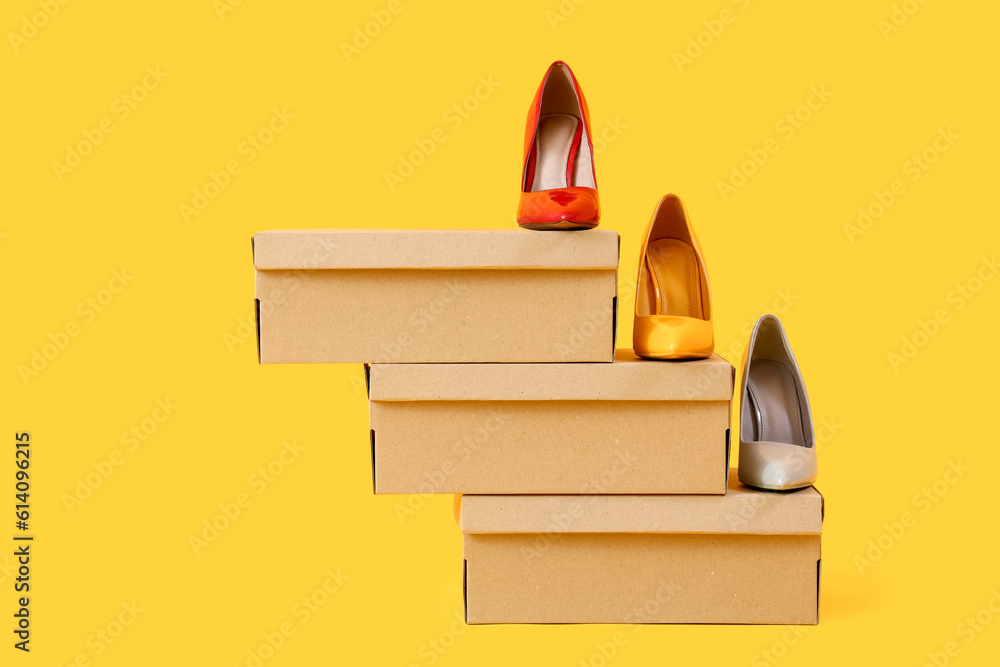 Cardboard boxes with different stylish high-heeled shoes on yellow background