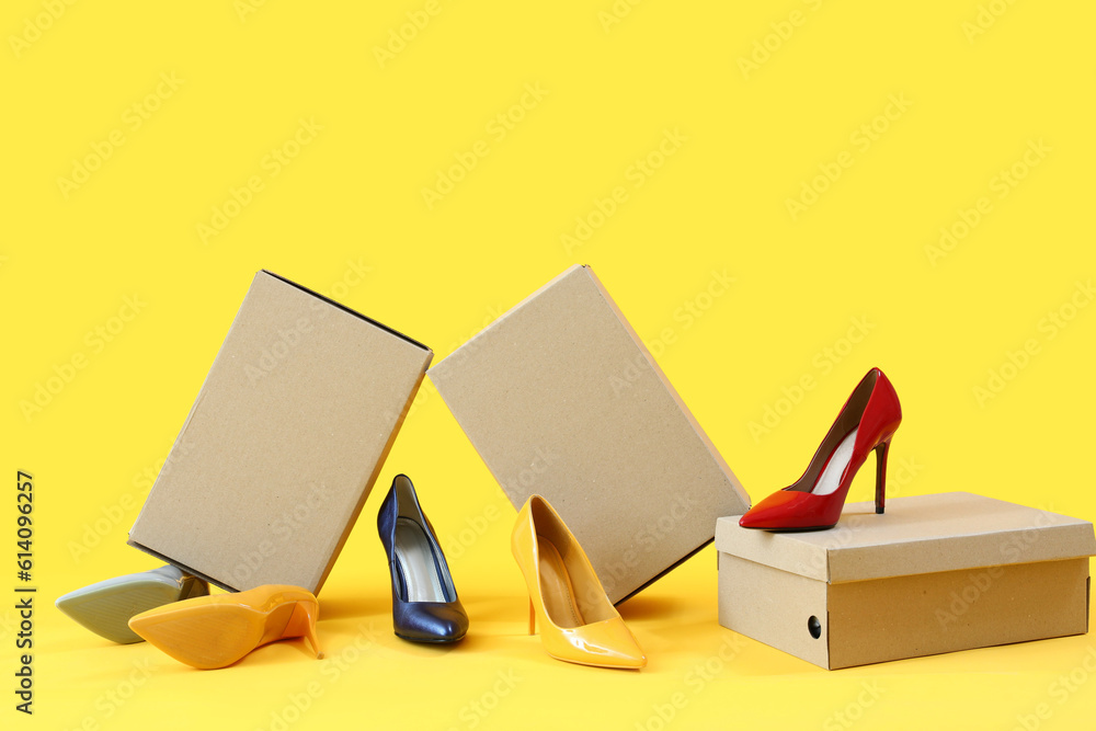 Cardboard boxes with different stylish high-heeled shoes on yellow background