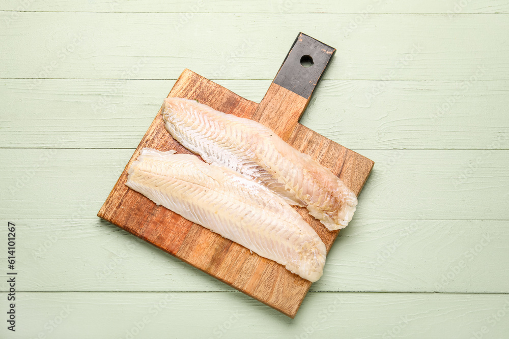 Board with raw codfish fillet on green wooden background